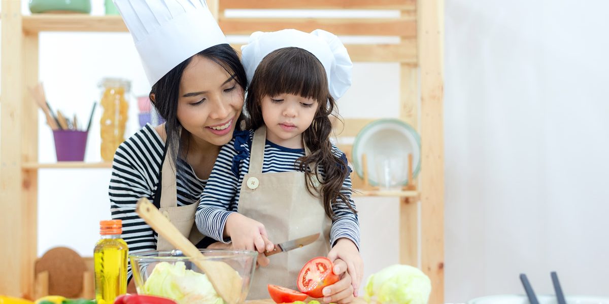 A mother and her daughter cooking while wearing chef hats